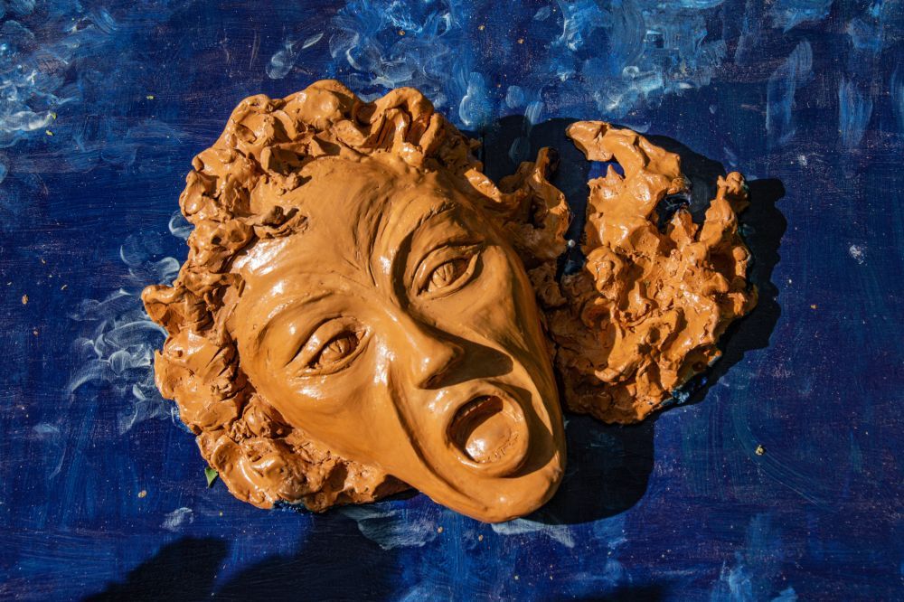 Il volto, rivolto verso l'alto nell'atto di urlare, emerge da una lastra dipinta di blu intenso che raffigura il mare. I capelli, resi con una materia grezza e mossa, si confondono con la spuma delle onde che li circonda, in un'unica compenetrazione tra figura umana e paesaggio marino.